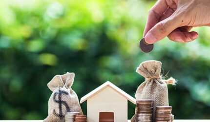 Saving money, home loan, mortgage, a property investment for future concept : A man hand putting money coin over small residence house and money bag.